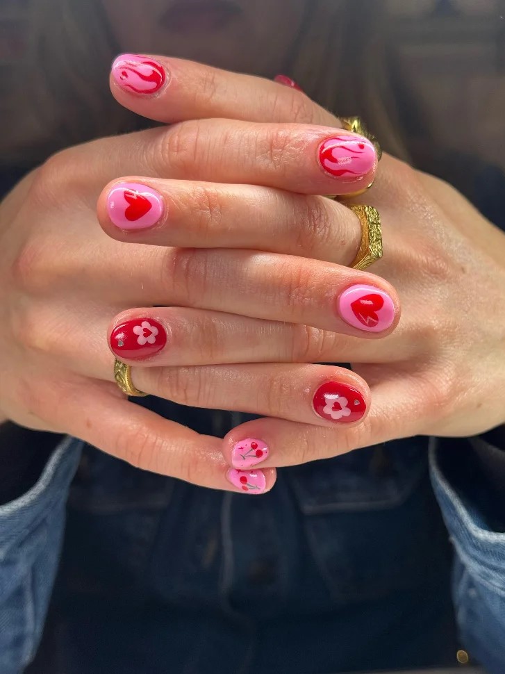 Manos de mujer entrelazadas con una manicura BIAB en rosa intenso y rojo con nail art