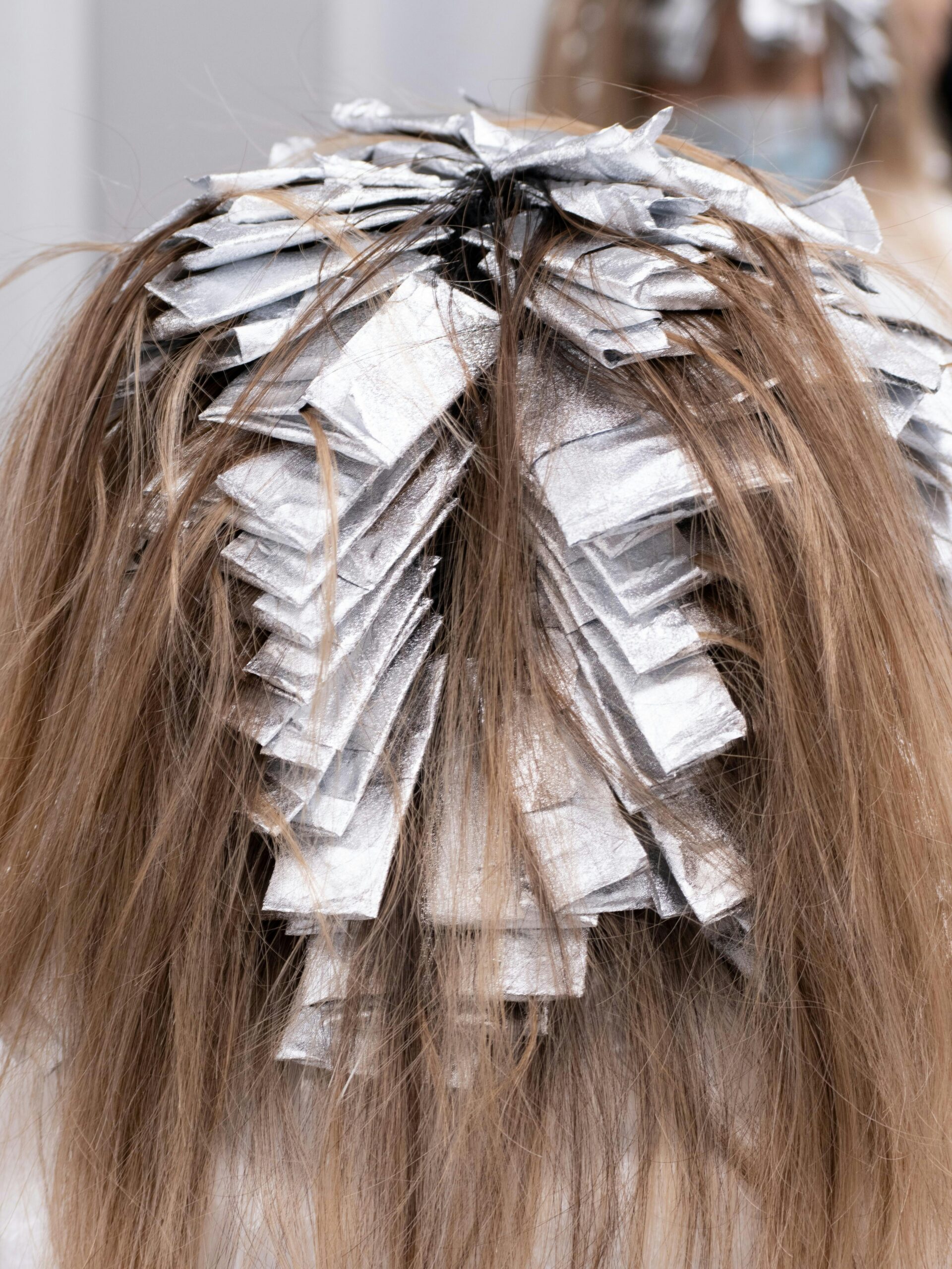 Parte trasera de la cabeza de una clienta con papeles de mechas durante un tratamiento de coloración parcial en la peluquería