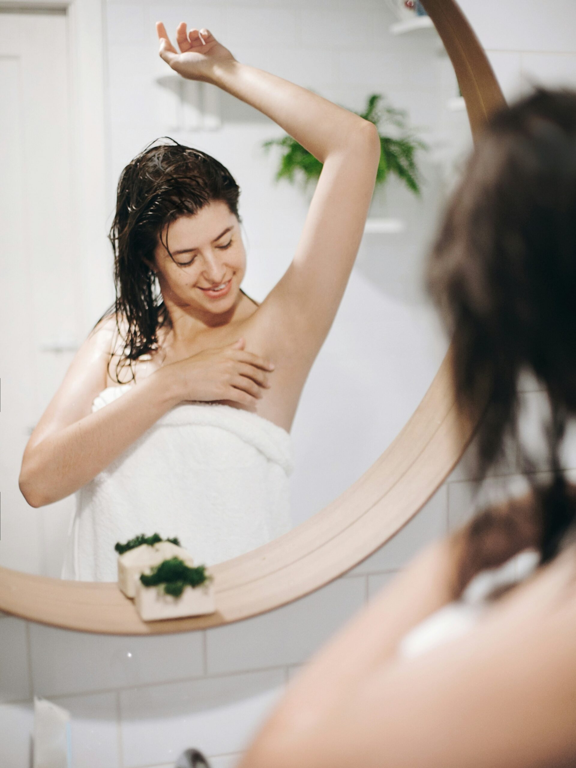 Mujer con una toalla de baño admirando sus axilas suaves en el espejo después de un tratamiento de IPL