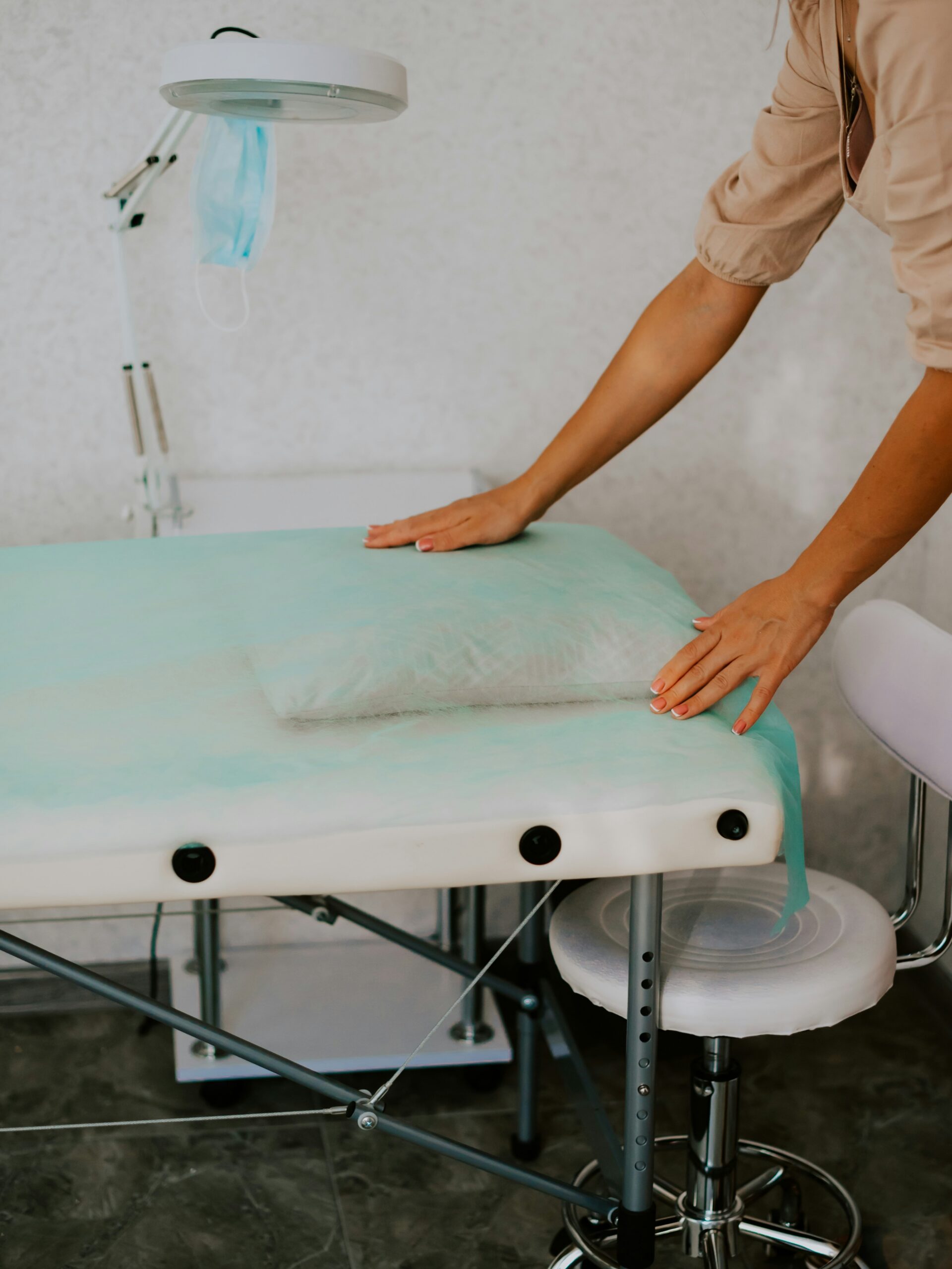 Una sala de tratamiento en un centro de estética limpia e higiénica, con una profesional colocando una sábana limpia sobre la camilla