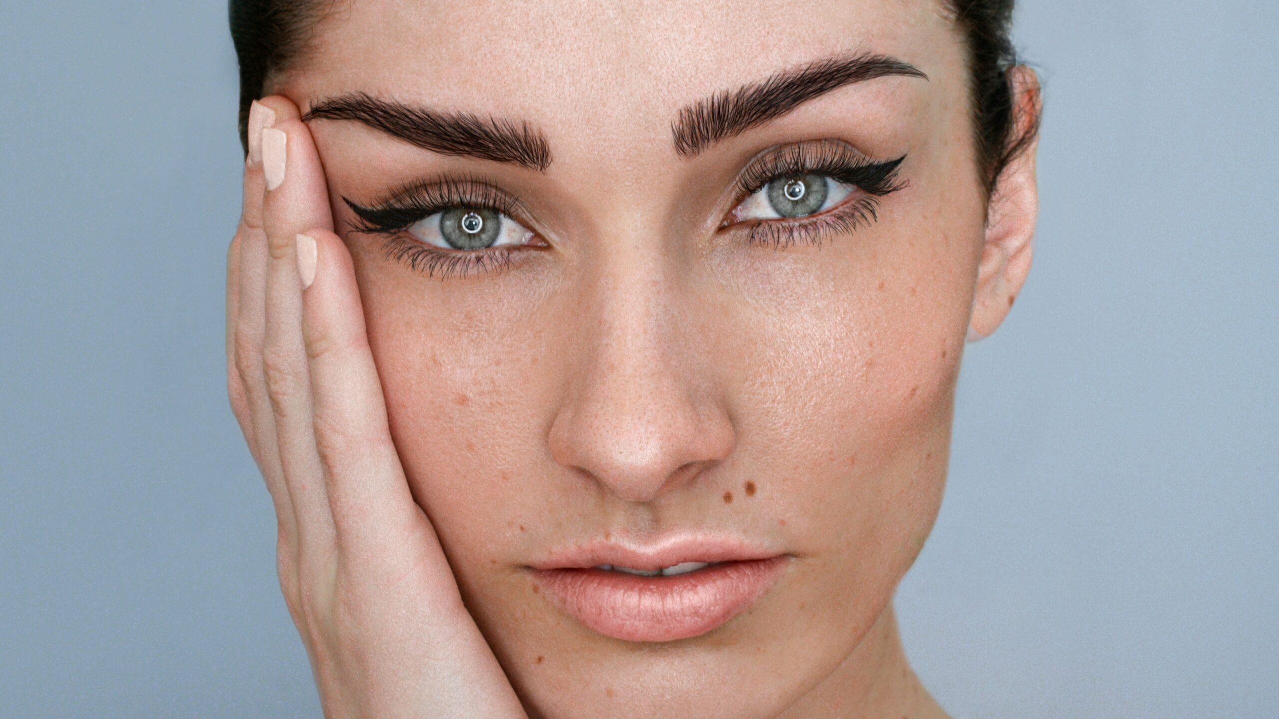 Primer plano del rostro de una mujer con microblading en las cejas, maquillaje natural y el pelo oscuro recogido