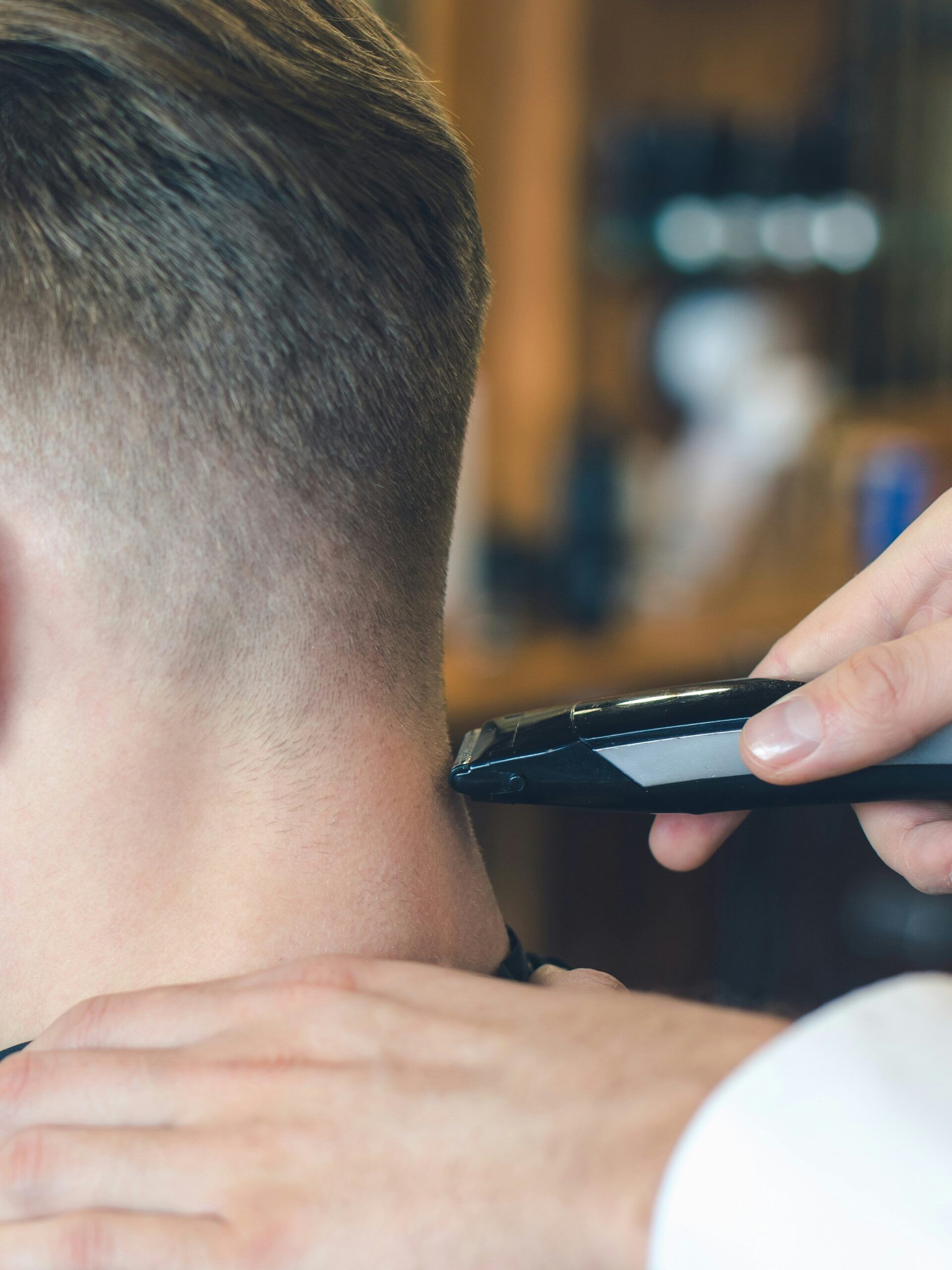 Primer plano de un barbero realizando un taper fade con maquinilla en la parte posterior de la cabeza de un cliente con cabello liso