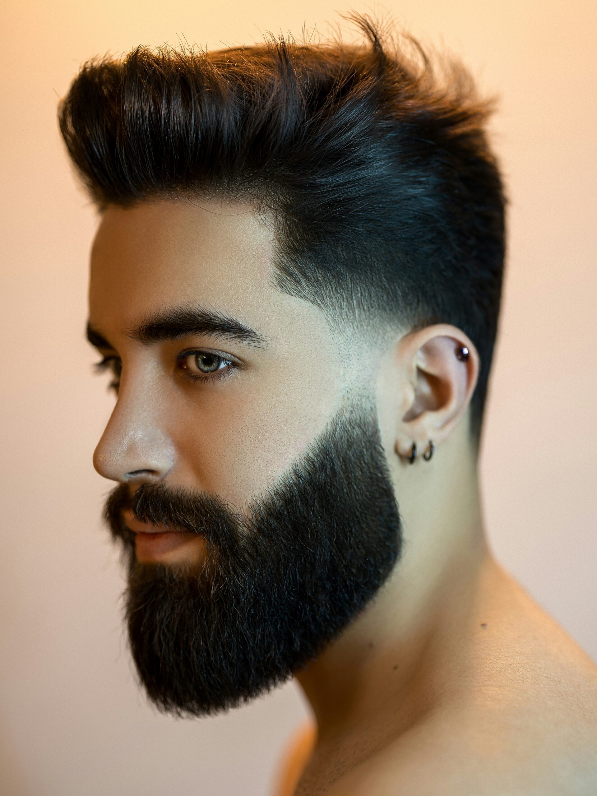 Hombre con rostro ovalado y cabello oscuro con un low taper fade voluminoso y barba