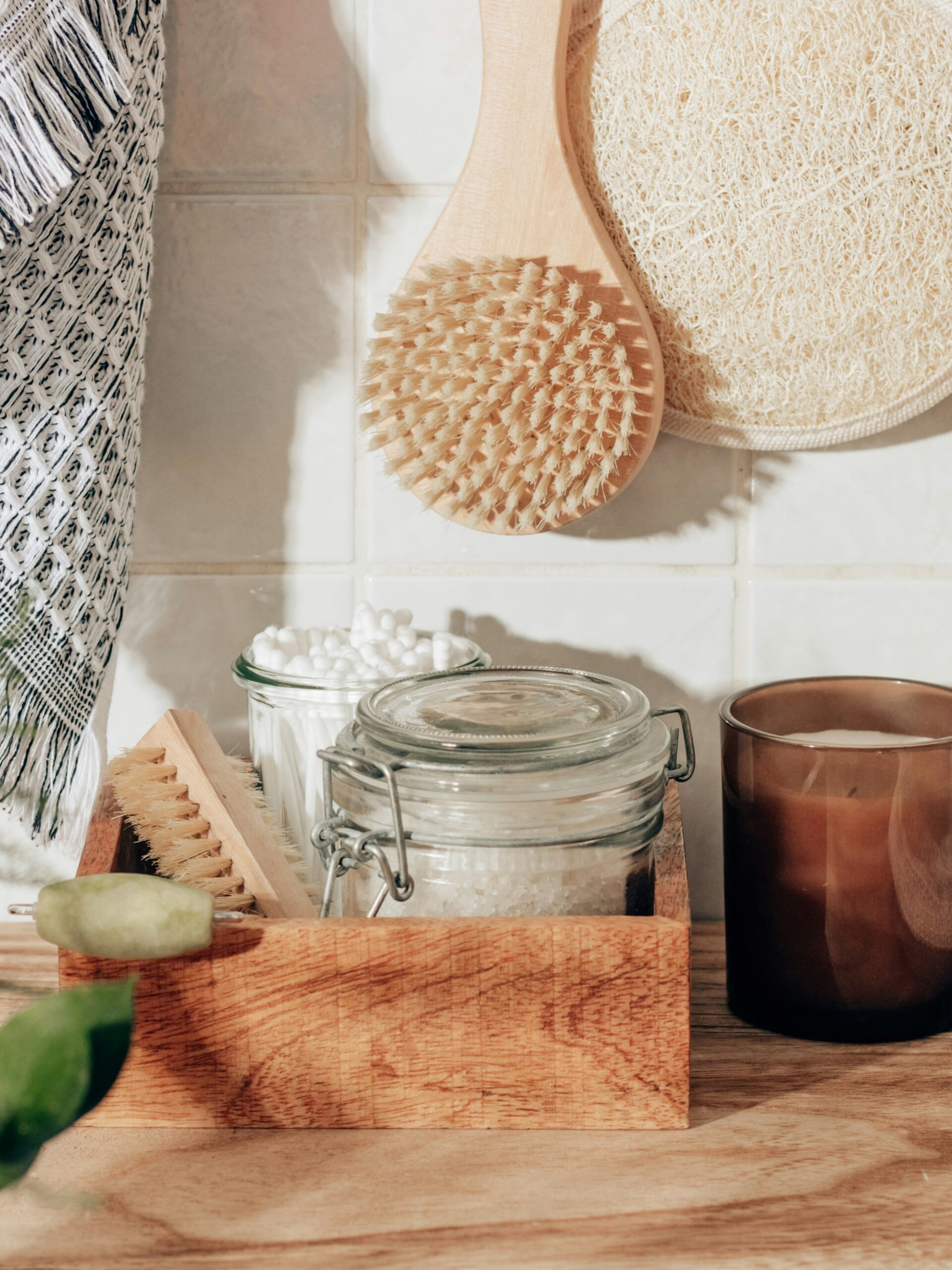 Bodegón de accesorios de baño: un guante exfoliante, un cepillo corporal, sales de baño, bastoncillos de algodón y una vela