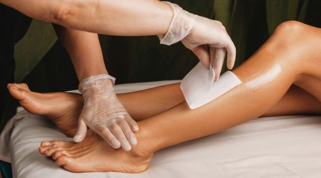 Primer plano de una esteticista depilando con cera la parte inferior de la pierna de una clienta en un salón luminoso y limpio