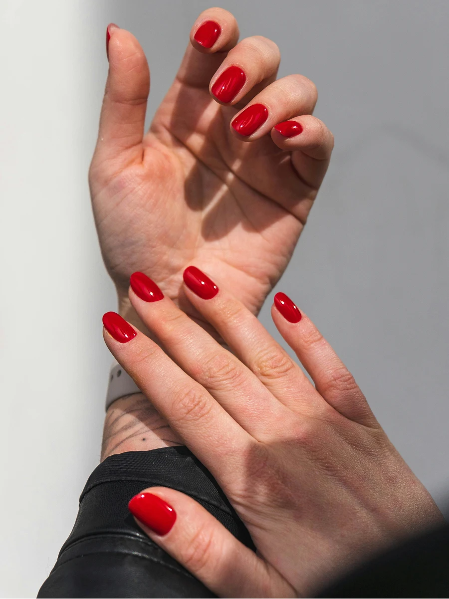 Primer plano de los antebrazos de una mujer con una chaqueta de cuero negra que luce una manicura de gel roja y brillante