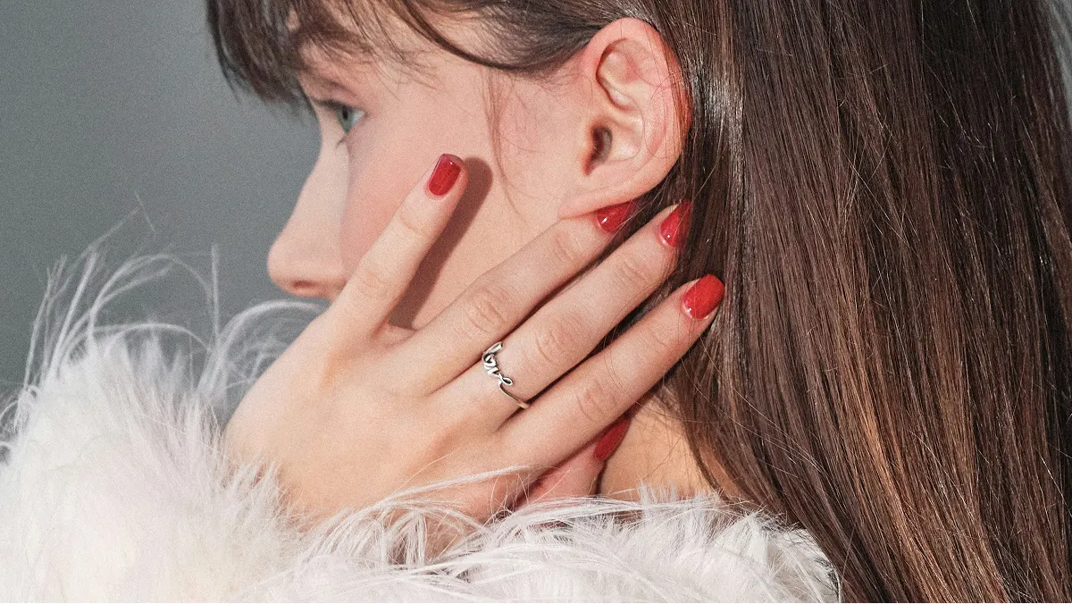 Primer plano de perfil de una mujer morena que se toca la cara y luce una manicura de gel roja y brillante