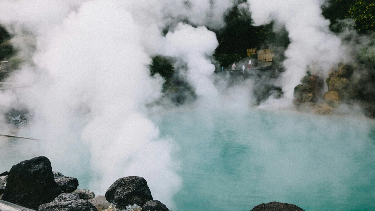 Vista amplia de unas aguas termales en Japón con nubes de vapor que se elevan de una poza rodeada de rocas y vegetación