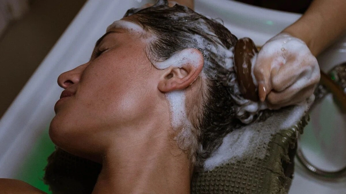 Primer plano de un terapeuta realizando un head spa japonés con un cepillo para el cuero cabelludo a una clienta
