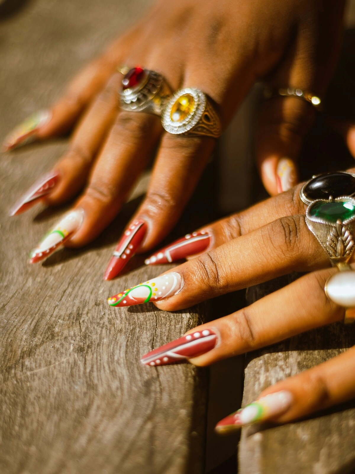 Primer plano de las manos de una mujer con uñas acrílicas stiletto en rojo y blanco, decoradas con puntos y espirales verdes y amarillos