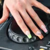 Una mano con la electric mani sobre el jog wheel de un plato de DJ Pioneer, con puntas francesas de neón en animal print y espirales