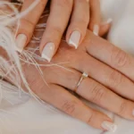 Manicura francesa clásica en blanco sobre uñas naturales de forma cuadrada, sobre una tela blanca