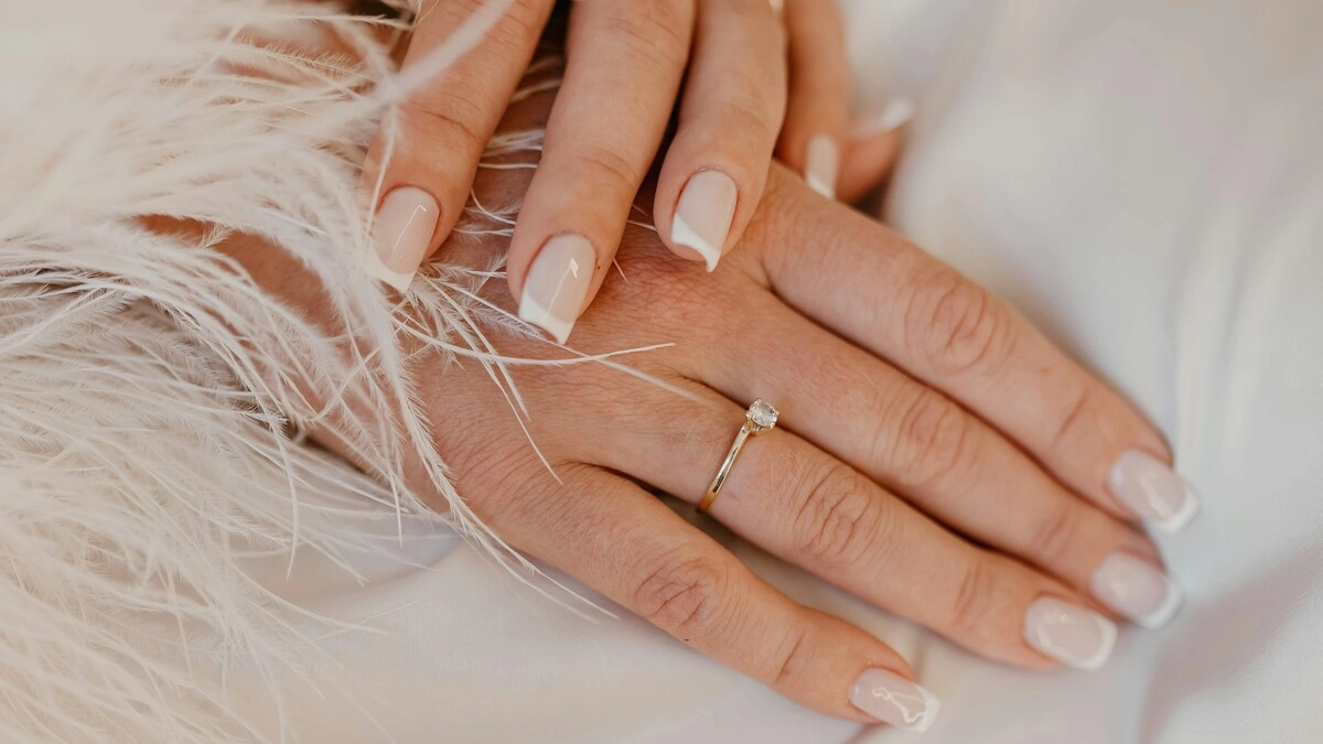 Manicura francesa clásica en blanco sobre uñas naturales de forma cuadrada, sobre una tela blanca