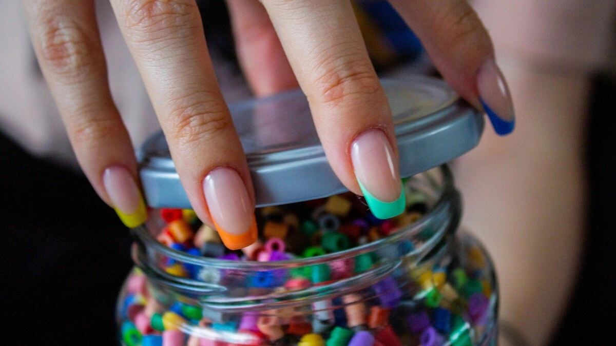 La mano de una mujer con una manicura francesa con base nude transparente y puntas de varios colores
