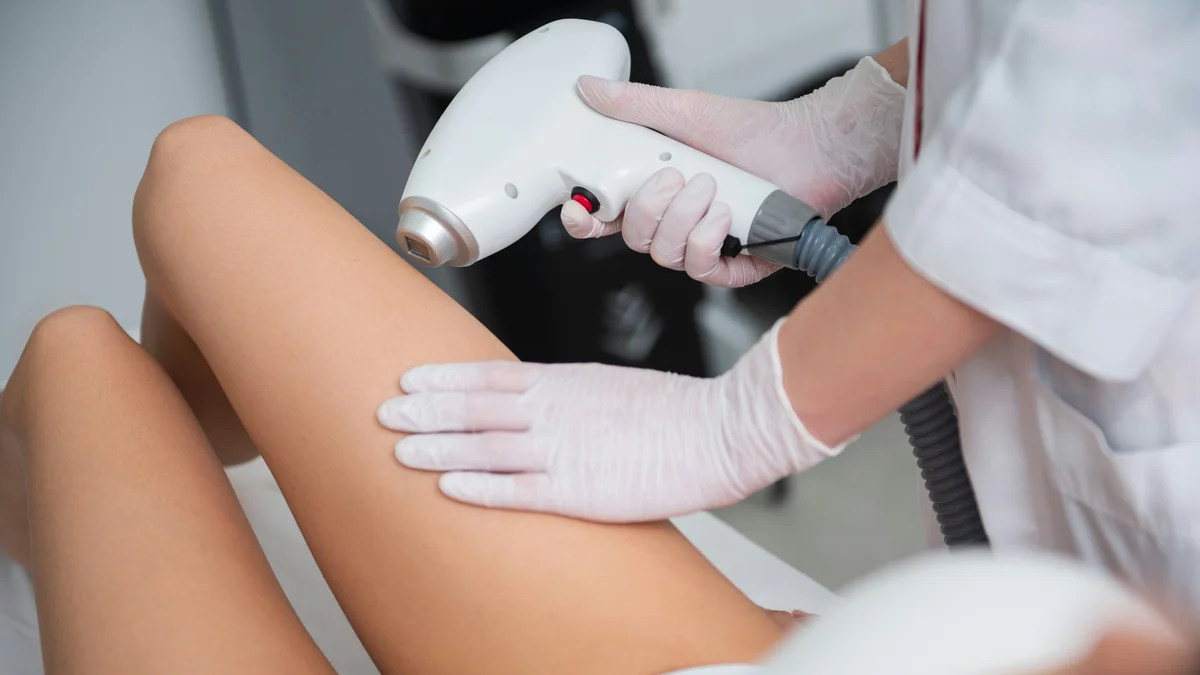 Primer plano de una esteticista tratando la parte inferior de la pierna de una clienta durante una sesión de depilación láser