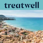 Vista panorámica de un pueblo costero siciliano, con antiguos edificios de tejados de terracota, una media luna de playa de arena, un mar turquesa cristalino y un promontorio rocoso que se alza a un lado.