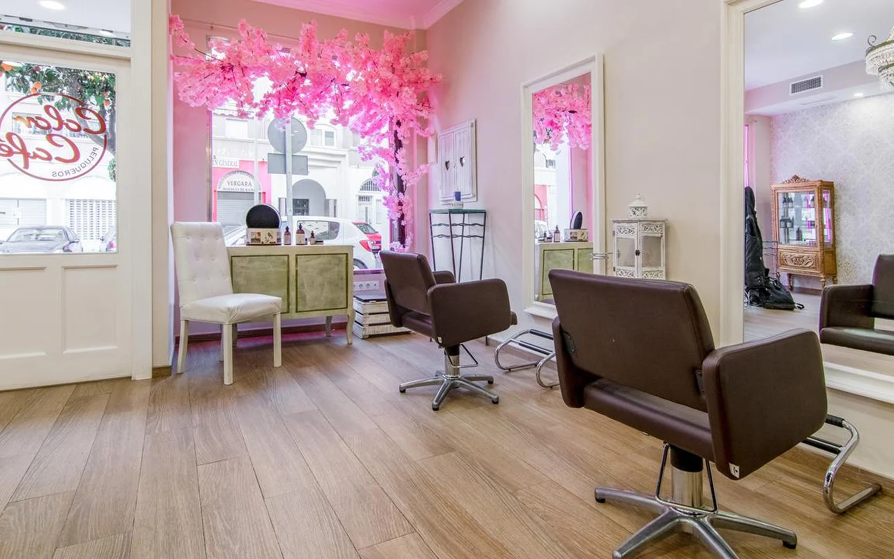 El interior de Color Café Peluqueros en Torremolinos, una peluquería de paredes rosas con sillas de peinado marrones, grandes espejos y una exposición de cerezo en flor rosa en el escaparate.