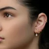 Foto de estudio de una mujer con varios piercings en el lóbulo y un aro en el hélix formando un ear look