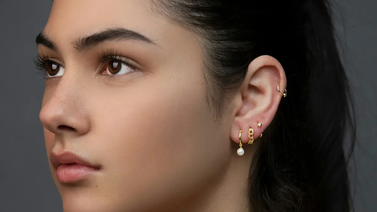 Foto de estudio de una mujer con varios piercings en el lóbulo y un aro en el hélix formando un ear look