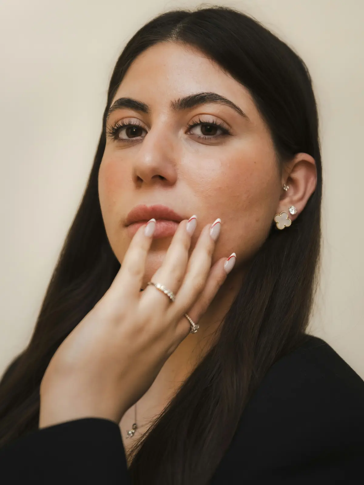 Foto de estudio de una mujer con piercings en el lóbulo y el tragus, con una mano de manicura cuidada apoyada en la cara