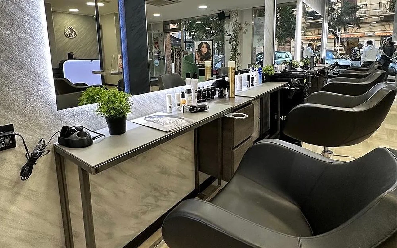 La zona de peinado de Equipe Beauty, con una fila de sillones negros a lo largo de una encimera efecto mármol, un gran espejo retroiluminado, productos de peinado y una planta en maceta sobre la encimera, y ventanales del suelo al techo que dan a la calle.
