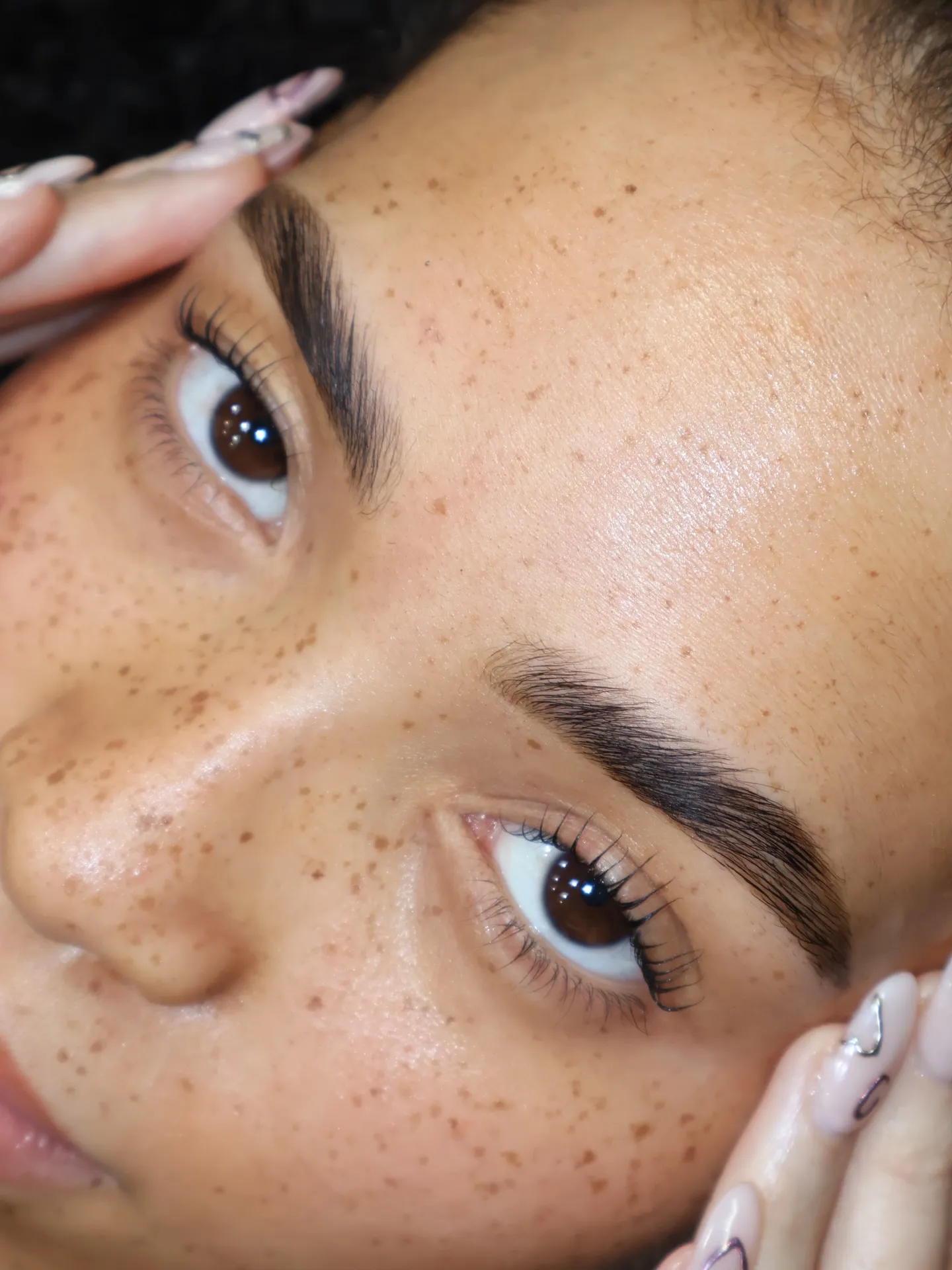 Primer plano de pestañas con efecto lifting natural tras un lifting de pestañas coreano, curvatura suave y bien separada de aspecto ligero, sobre una piel con pecas