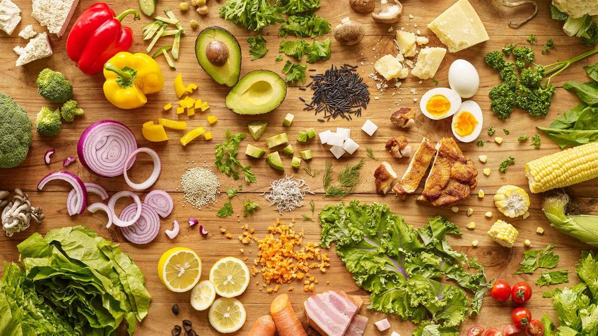 Vista cenital de una encimera de madera cubierta de alimentos nutritivos y coloridos: huevos, verduras, ensalada y pollo