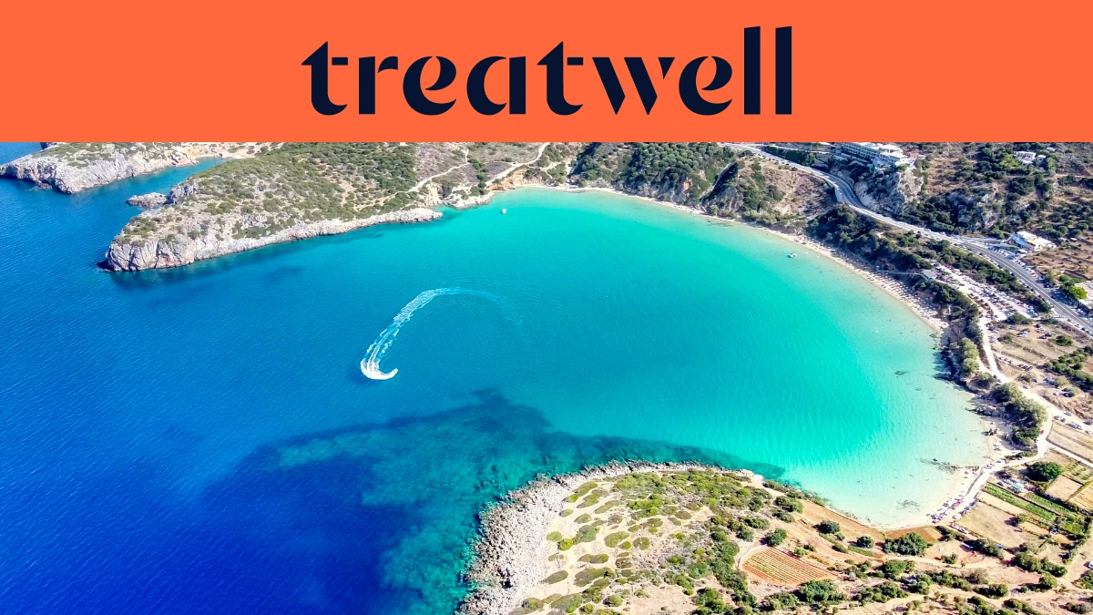 Vista aérea de una bahía cretense turquesa, con una moto de agua trazando una curva blanca por el agua clara, una media luna de playa de arena y colinas secas alrededor de la orilla, bajo un banner naranja coral con la palabra treatwell.