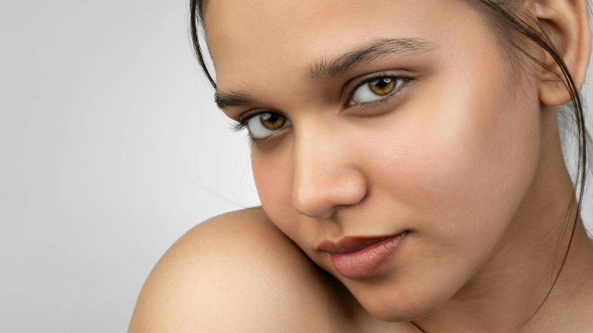 Primer plano de una mujer sonriendo a la cámara que muestra su piel suave y sin maquillaje