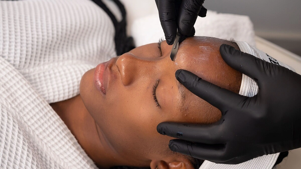 Primer plano de una esteticista realizando dermaplaning a una clienta en un centro de belleza