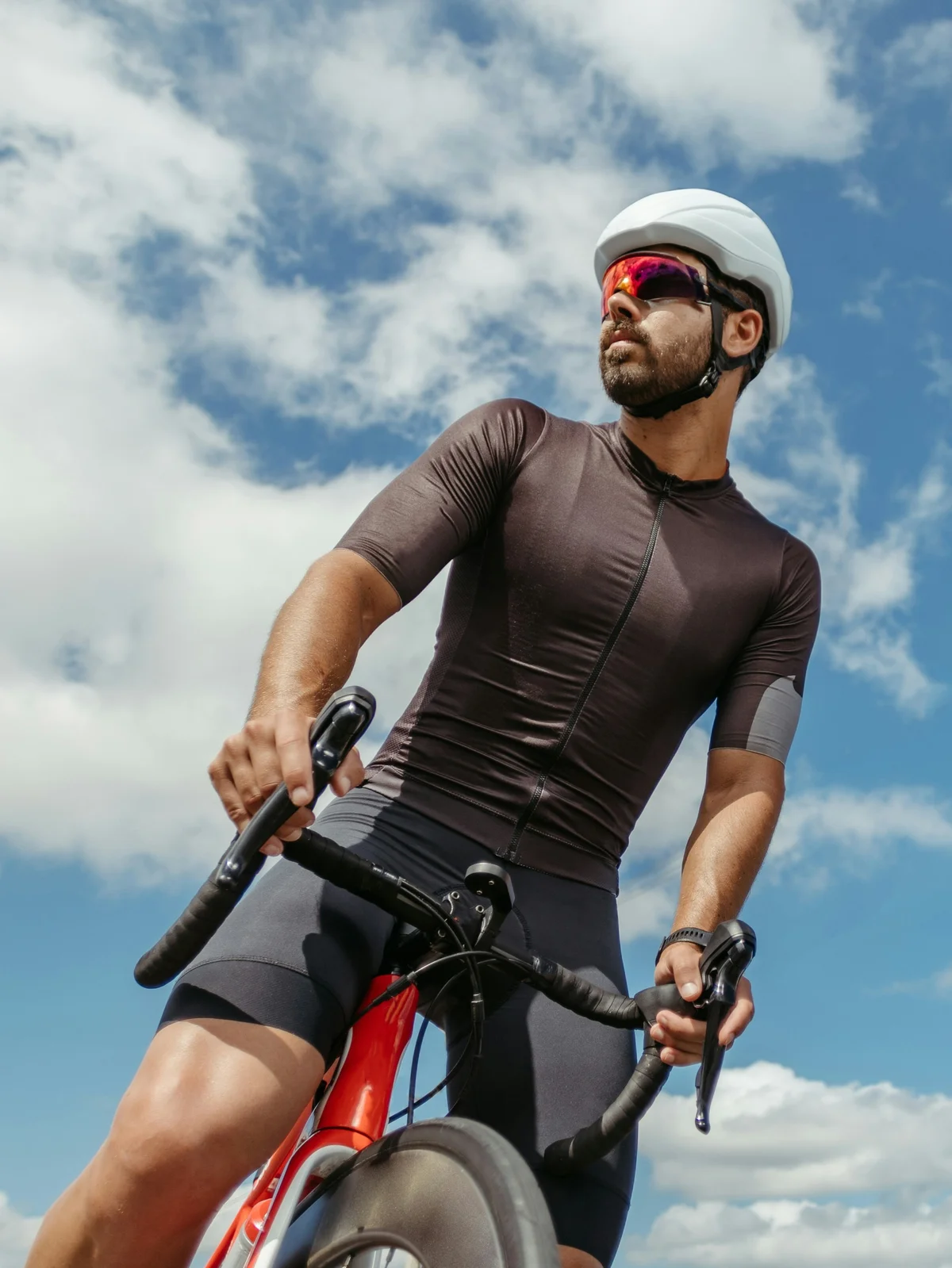 Tomado desde abajo, un ciclista a horcajadas sobre su bici se detiene a mirar a su alrededor bajo un cielo azul con nubes