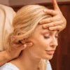 Primer plano de una mujer con los ojos cerrados mientras una profesional, durante un masaje indio de cabeza, le apoya una mano en la frente y con la otra le masajea el cuello