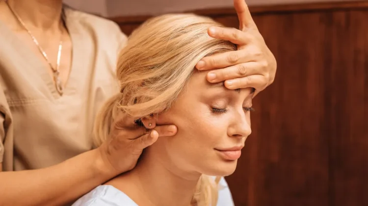 Primer plano de una mujer con los ojos cerrados mientras una profesional, durante un masaje indio de cabeza, le apoya una mano en la frente y con la otra le masajea el cuello