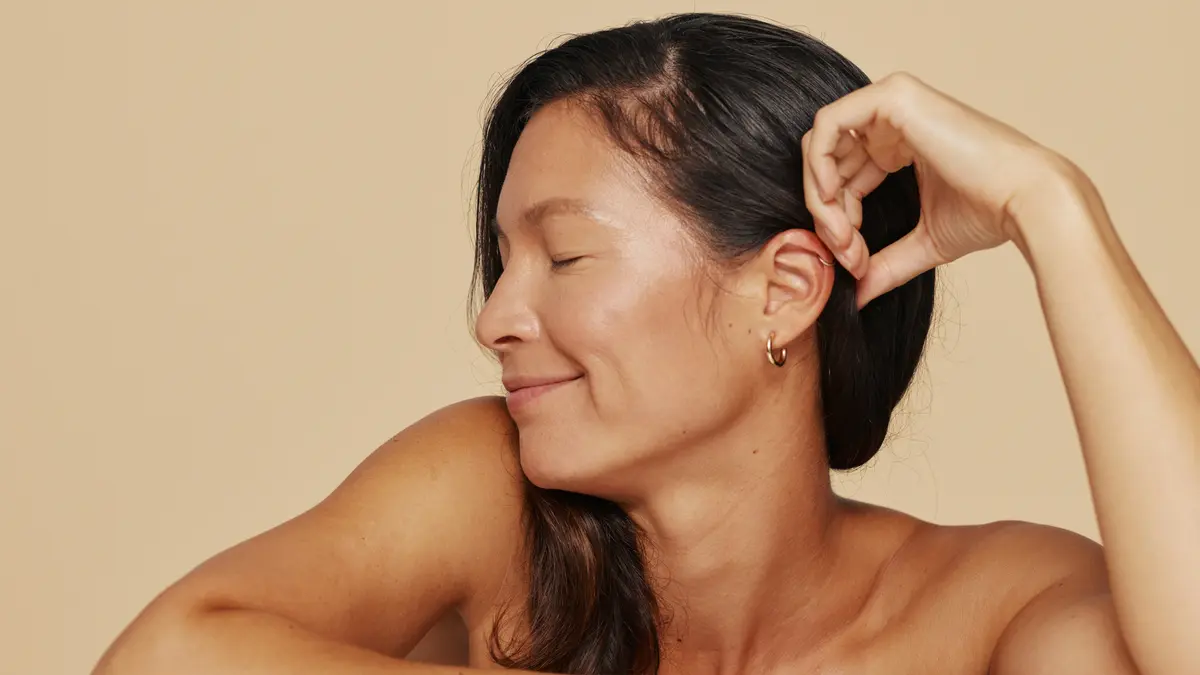 Mujer de hombros para arriba, sonriente con los ojos cerrados, relajada y descansada mientras mira hacia un lado
