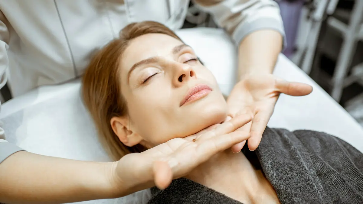 Mujer relajada durante un masaje facial de drenaje linfático suave, con las manos de la profesional deslizándose ligeras bajo su mandíbula
