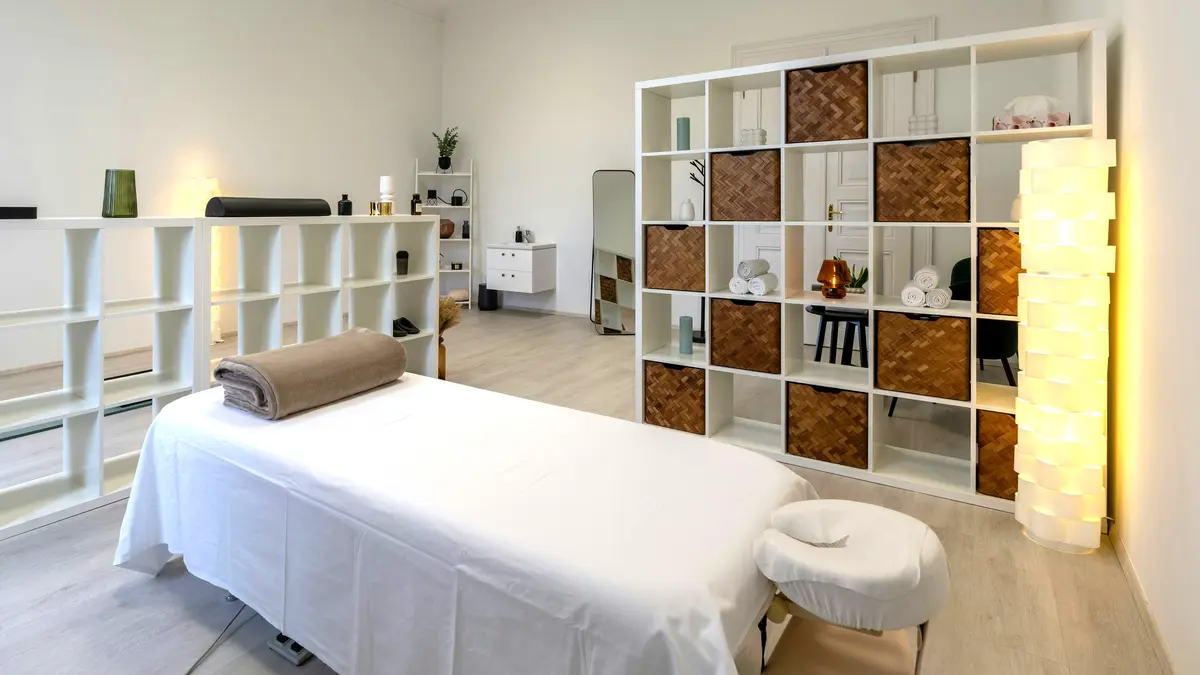 Cabina de tratamientos limpia y ordenada en un centro de estética, con la camilla preparada con sábanas y una manta enrollada, lista para un masaje