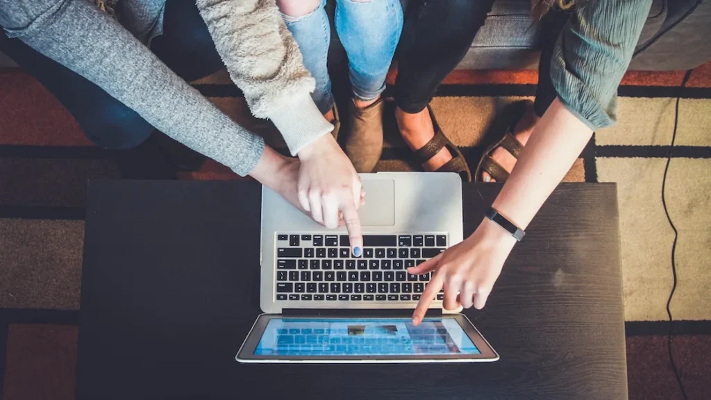 Tres personas reunidas alrededor de un portátil, señalando la pantalla mientras navegan juntas por internet.