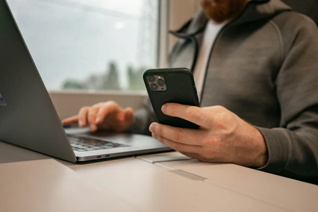 Un propietario de salón gestiona las reservas online desde el móvil mientras usa el portátil