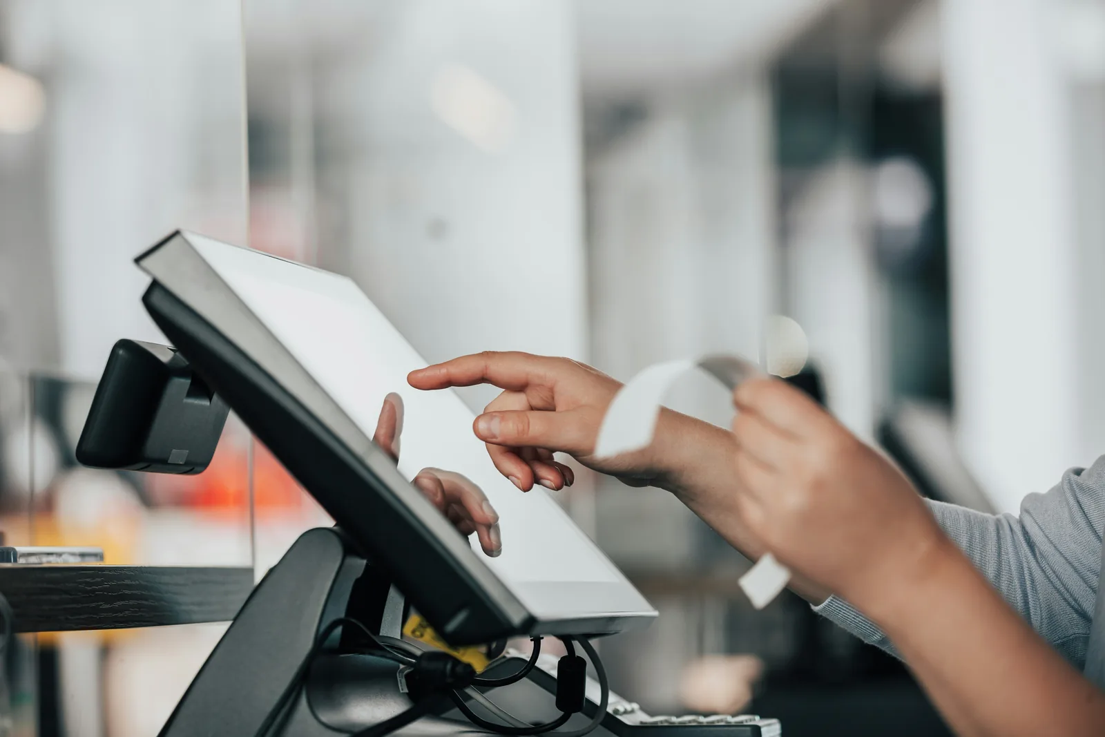 Unas manos utilizan un sistema de punto de venta táctil en el mostrador y cortan un recibo impreso